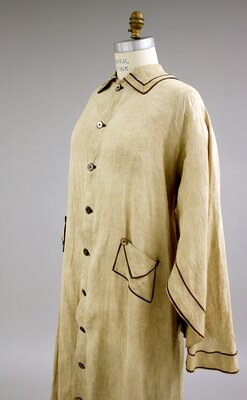 Early twentieth-century caped duster, tan with brown piping (quarter view)). 